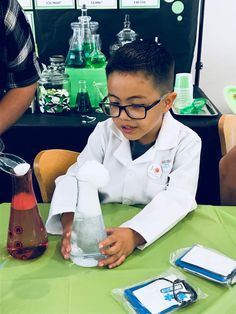 a young boy in white lab coat sitting at table with flasks