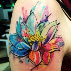 a colorful flower tattoo on the back of a woman's shoulder, with watercolors all over it