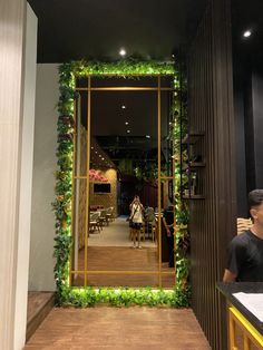 a man sitting at a table in front of a mirror with greenery on it