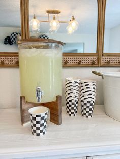 a beverage dispenser sitting on top of a counter next to two cups