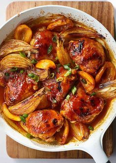 a pan filled with chicken and onions on top of a wooden cutting board