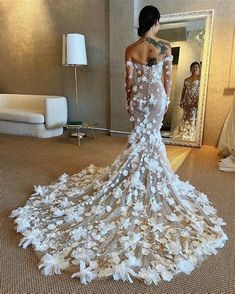 a woman standing in front of a mirror wearing a wedding dress with flowers on it