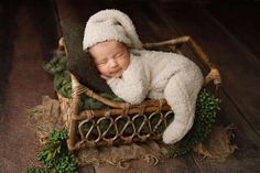 a newborn baby wrapped in a white bunny outfit is sleeping on a wicker basket