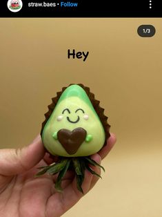 someone is holding a tiny green object with a heart on it's face and the word hey written below