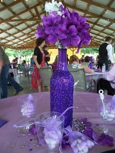 a purple vase filled with flowers sitting on top of a table next to wine glasses