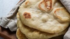 a stack of flat bread on top of a wooden cutting board next to a cloth