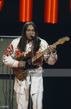 a man with long hair playing guitar on stage