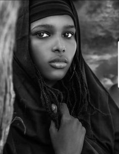 a woman with dreadlocks standing in front of a dark sky and clouds, looking at the camera