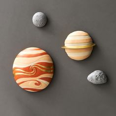 three different sized planets on a gray surface next to two rocks and one is painted orange