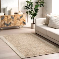 a living room with a couch, rug and potted plant on the sideboard