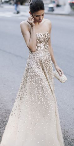 a woman in a long dress is talking on her cell phone while walking down the street