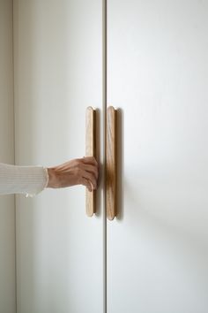 a person's hand on the door handle of a white cabinet with wood handles