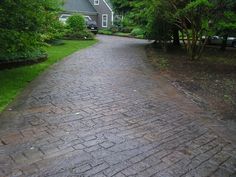 a brick path in front of a house with trees on both sides and cars parked at the end