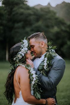 a bride and groom embracing each other with greenery around their necks in front of mountains