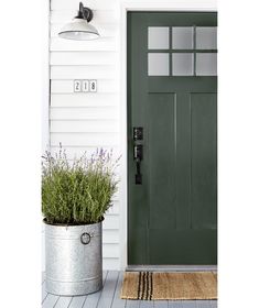 a green front door on a white house next to a planter with lavender in it