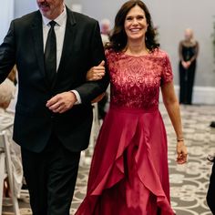 a woman in a red dress walking next to a man in a black suit and tie