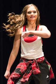 a woman in red and white shirt doing a dance move with her hair blowing in the wind