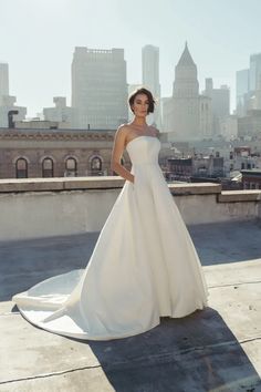 a woman in a white wedding dress standing on a roof with the city skyline behind her