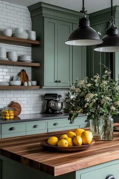 a bowl of lemons sits on a kitchen counter with green cabinets and hanging lights