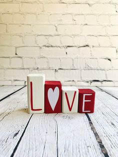 the word love spelled with wooden blocks in front of a brick wall and whitewashed wood floor