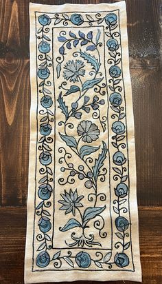 an embroidered table runner with blue flowers and leaves on it, against a wooden background