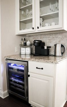 a kitchen with white cabinets and an open wine cooler in the corner next to it