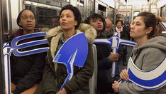 several people sitting on a subway train with their backs to each other and holding up signs