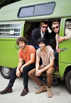 four men are sitting in the open door of a green vw camper van