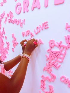 a woman writing on a white wall with pink letters in the shape of words and numbers