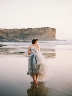 a woman standing on top of a beach next to the ocean wearing a blue dress