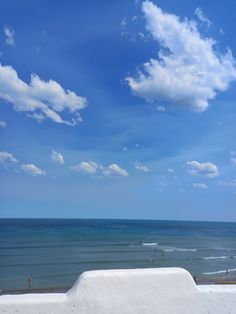 a bench sitting on top of a cement wall next to the ocean under a cloudy blue sky