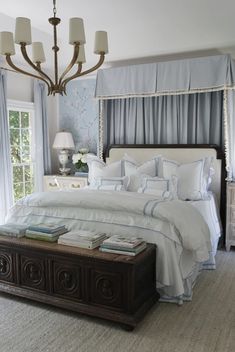 a white bed sitting under a chandelier in a bedroom next to a window