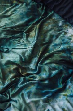 a blue and green tie - dyed blanket laying on top of a black bed sheet