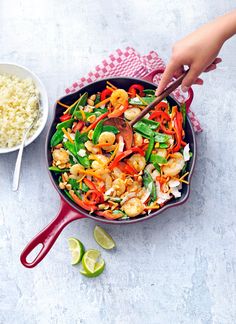 a pan filled with shrimp and vegetables next to a bowl of rice