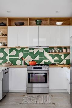 a kitchen with white cabinets and green patterned backsplashing on the wall above the stove