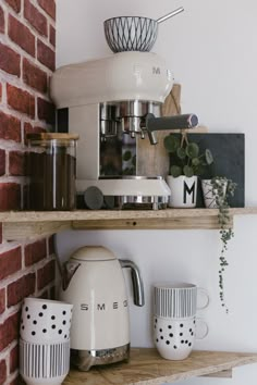 some coffee cups are sitting on the shelf in front of a brick wall and there is an espresso machine next to it