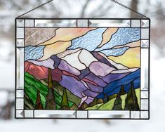 a stained glass window hanging from the side of a building with mountains in the background