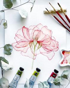 watercolors, paint and brushes are arranged on a sheet of paper next to some flowers