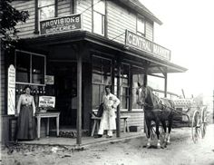 an old black and white photo of two people standing in front of a small store