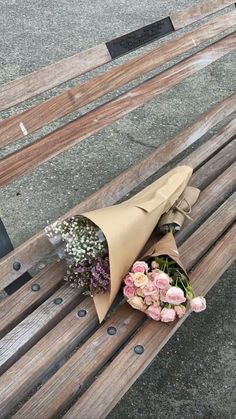 a bouquet of flowers is wrapped in brown paper on a wooden park bench with metal studs