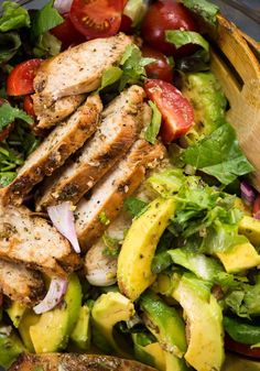 a salad with chicken, lettuce, tomatoes and avocado in it