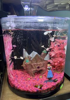 a fish tank filled with pink plants and other items on top of a wooden table