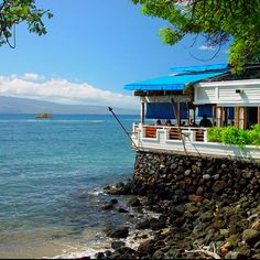 a house sitting on top of a rocky cliff next to the ocean with a boat in the distance