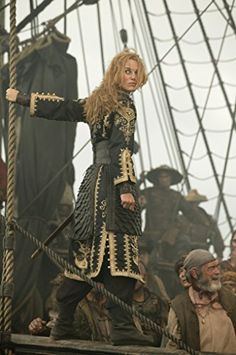 a woman dressed in black and gold standing on top of a boat with her arms outstretched