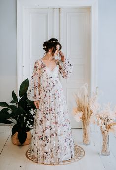 a woman standing in front of a door wearing a white dress with flowers on it