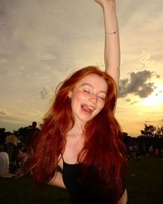 a woman with red hair is smiling and raising her arms in the air at sunset