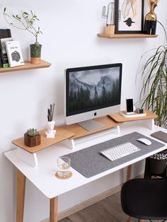 a white desk with a computer monitor and keyboard on it next to a potted plant