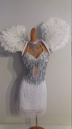 a mannequin with white feathers and silver beads on it's chest, in front of a wall