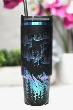 a black and blue tumbler cup with an aurora bore design on the side, in front of pink flowers