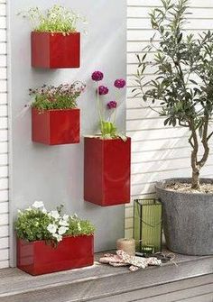 three red planters with flowers in them on a shelf